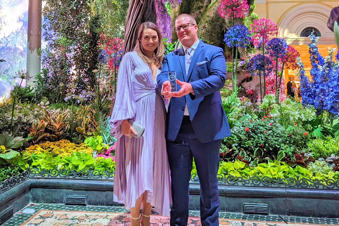Stephanie and David Hayes standing side by side while David holds out a trophy in his hands.