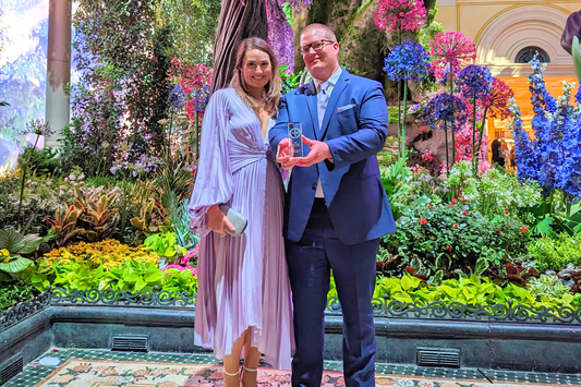 Stephanie and David Hayes standing side by side while David holds out a trophy in his hands.